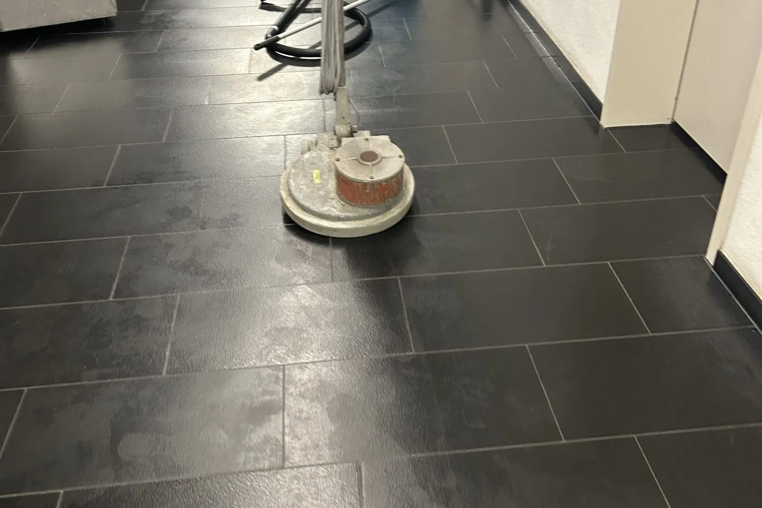 Einscheibenmaschine auf einem dunklen Fliesenflur während der Grundreinigung